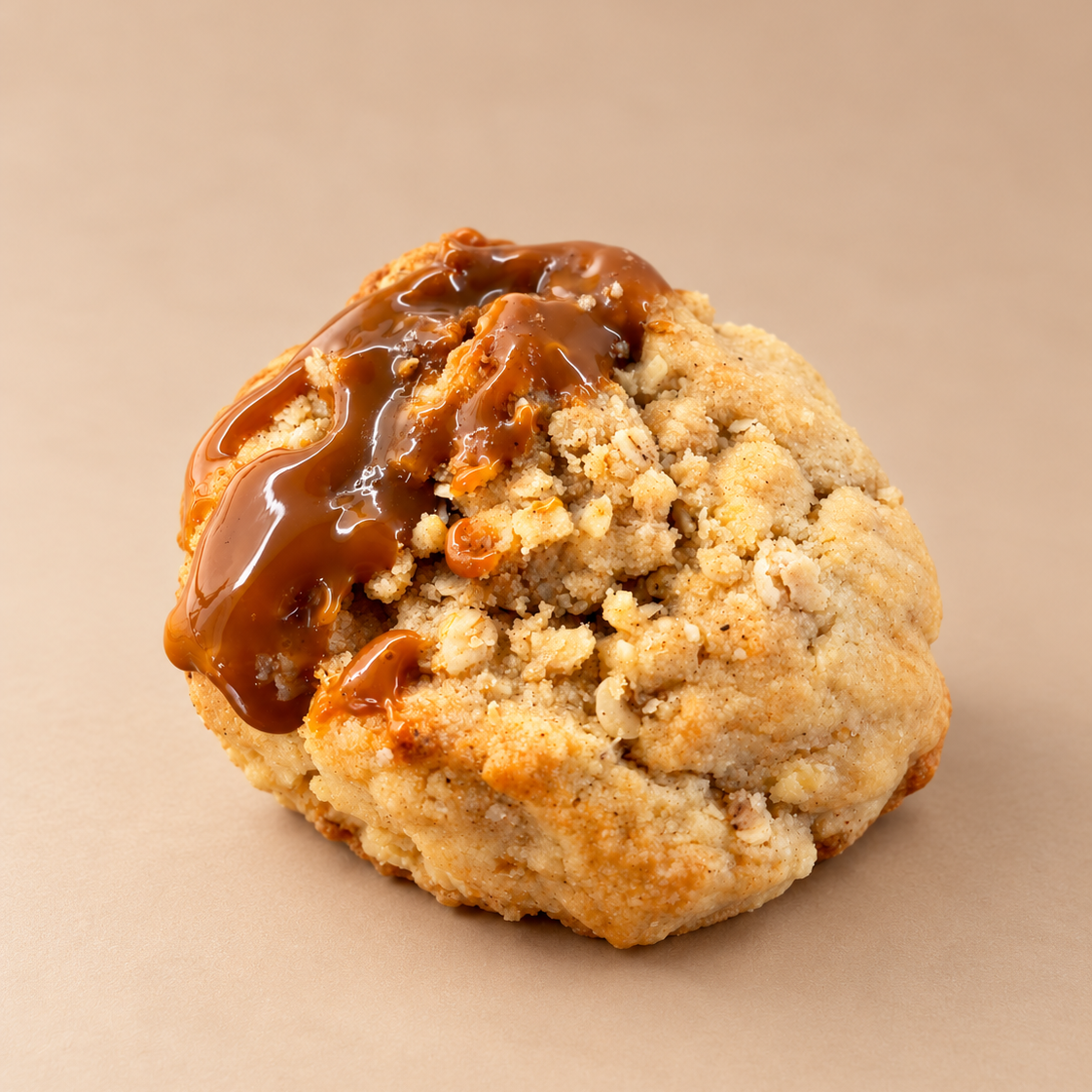A single baked cookie with a crumbly golden-brown texture and glossy salted caramel drizzle on top, apple crumble cookie with salted caramel perfect for autumn evenings.