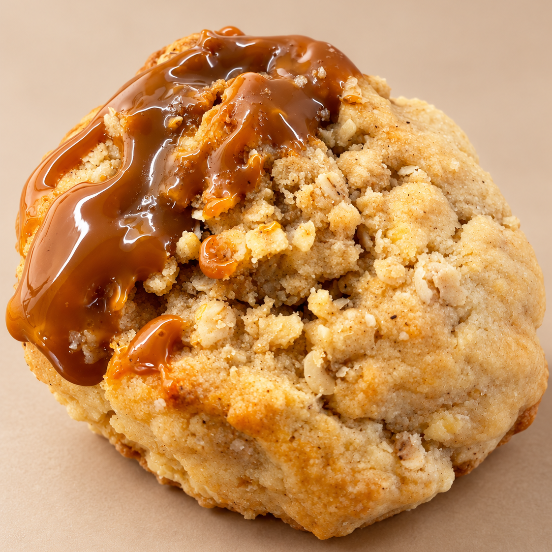 A close-up of a golden-brown baked apple crumble cookie topped with salted caramel sauce, perfect for autumn